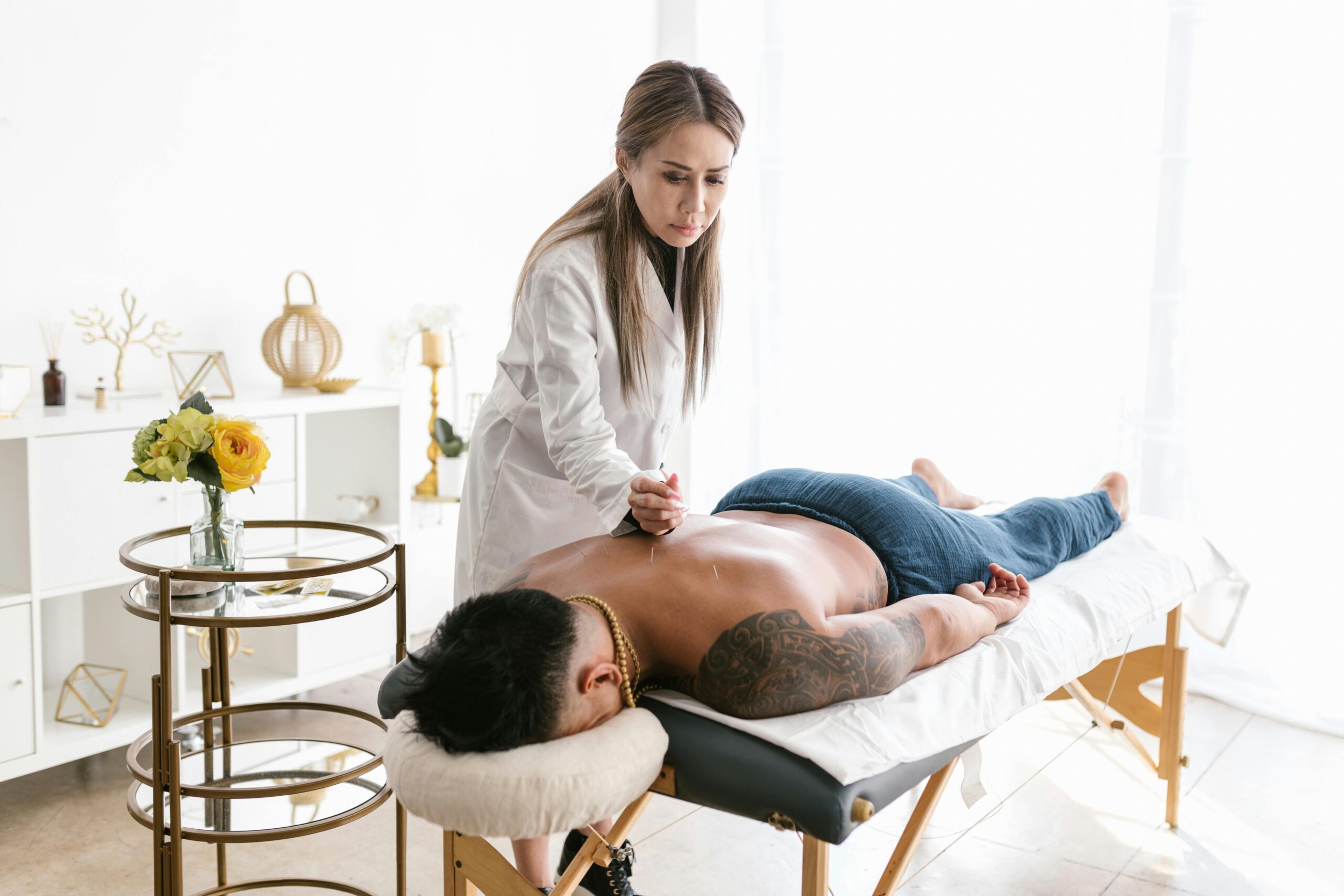 A white female doctor performs acupuncture on the back of a Black male patient